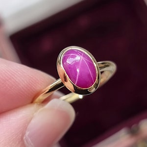Op de afbeelding: Een gouden ring met een roze ovale edelsteen in een bezel-setting.