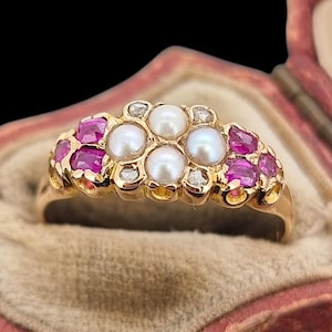 Può includere: Un anello vintage in oro con un design a grappolo. È adornato con cinque perle, pietre preziose rosa e piccoli diamanti. L'anello è presentato in un portagioie di velluto rosso su sfondo nero.