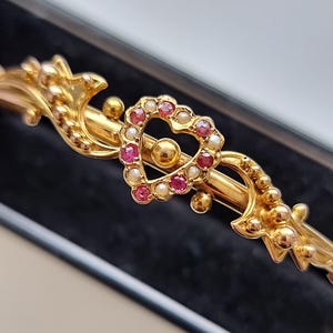 Pode incluir: Um bracelete de ouro com um design em forma de coração. O coração é adornado com pedras preciosas cor-de-rosa e pérolas brancas.
