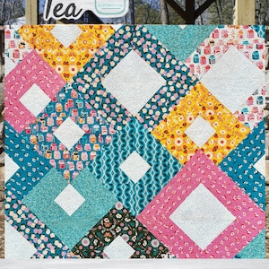 Könnte beinhalten: Ein farbenfroher Quilt mit einem geometrischen Muster. Der Quilt zeigt Rauten in verschiedenen Farben, darunter Rosa, Gelb und Türkis, mit weißen quadratischen Akzenten. Die Wörter "Sweet Tea" und "Dandelion Wishes 2" sind sichtbar.