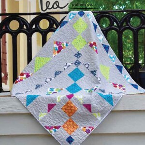 Könnte beinhalten: Ein Quiltmuster namens "Wacky Steps" von Sweet Tea pattern co. Der Quilt besteht aus grauem Stoff mit bunten geometrischen Formen in Blautönen, Grün, Rosa, Orange und Gelb.