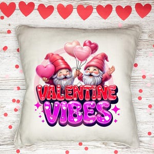 Könnte beinhalten: Ein weißes Kissen mit einem Valentinstag-Design mit zwei Gnomen, die rosa Herzen und Ballons halten. Der Text "VALENTINE VIBES" ist in rosa und lila Buchstaben.