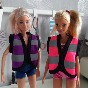 Puede incluir: Dos mu&ntilde;ecas con chalecos de seguridad. Una mu&ntilde;eca lleva un chaleco morado con rayas reflectantes grises y la otra mu&ntilde;eca lleva un chaleco rosa con rayas reflectantes grises.