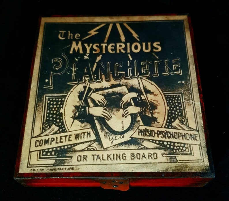 Puede incluir: Una caja de madera vintage con tapa roja y una etiqueta que dice "The Mysterious Planchette Complete with Physio-Psychophone or Talking Board." La etiqueta presenta una ilustraci&oacute;n en blanco y negro de manos que alcanzan una planchette.
