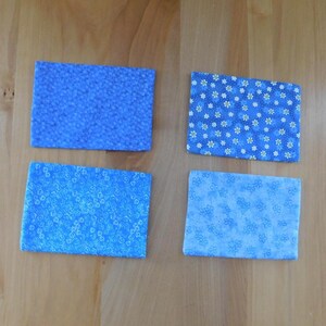 May include: Four rectangular fabric coasters featuring various blue floral patterns. The top left coaster has a dense blue floral print, the top right has white daisies on blue, the bottom left has small blue flowers, and the bottom right has light blue floral motifs.