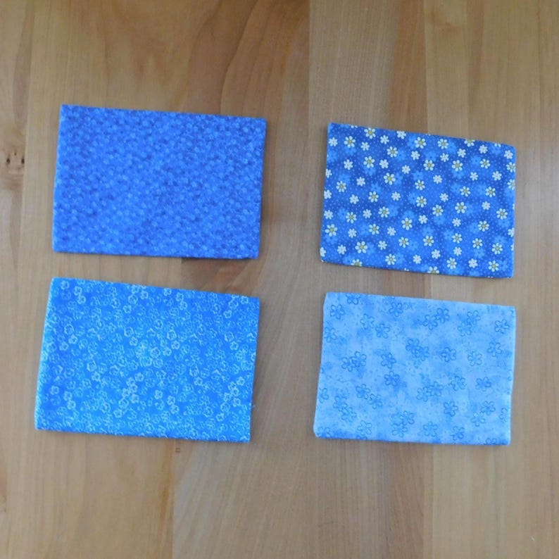 May include: Four rectangular fabric coasters featuring various blue floral patterns. The top left coaster has a dense blue floral print, the top right has white daisies on blue, the bottom left has small blue flowers, and the bottom right has light blue floral motifs.