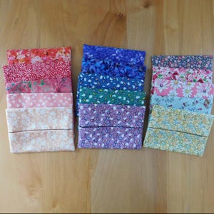 May include: A collection of rectangular fabric tissue holders arranged in three vertical stacks. The pouches feature various floral patterns in shades of red, pink, orange, blue, green, purple, and yellow, each with a horizontal center opening.