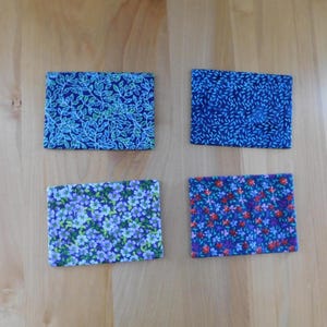 May include: Four rectangular fabric coasters featuring distinct patterns. The top left has a blue and green leaf print, the top right a blue dash pattern, the bottom left a purple floral print, and the bottom right a multi-coloured floral design.