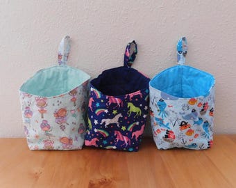 Peut inclure: Trois paniers de rangement suspendus en tissu avec des boucles. Le panier de gauche est bleu clair avec des illustrations de fées, celui du centre est bleu foncé avec des licornes et des arcs-en-ciel, et celui de droite est bleu clair avec des créatures marines pirates.