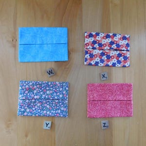 May include: Four rectangular fabric tissue holders labelled with wooden tiles W4, X6, Y4, and Z10. The top left is light blue with white swirls, the top right has red and blue flowers, the bottom left features small blue floral patterns, and the bottom right is solid pink.