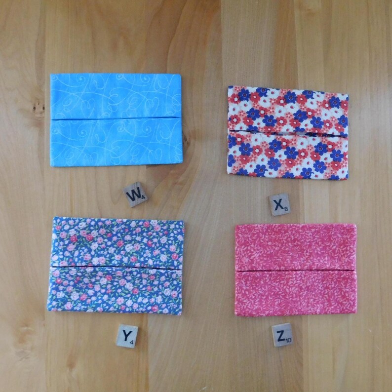 May include: Four rectangular fabric tissue holders labelled with wooden tiles W4, X6, Y4, and Z10. The top left is light blue with white swirls, the top right has red and blue flowers, the bottom left features small blue floral patterns, and the bottom right is solid pink.