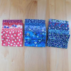 May include: Three stacks of rectangular fabric swatches featuring various floral patterns. The left stack displays shades of red and pink, the centre stack features blue and white floral designs, and the right stack shows dark blue and purple floral prints.