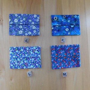 May include: Four rectangular fabric tissue holders featuring floral patterns. Top left J8 is purple with white flowers. Top right K5 is blue with white daisies. Bottom left L1 is light blue with tiny flowers. Bottom right M3 is dark blue with red and purple flowers.