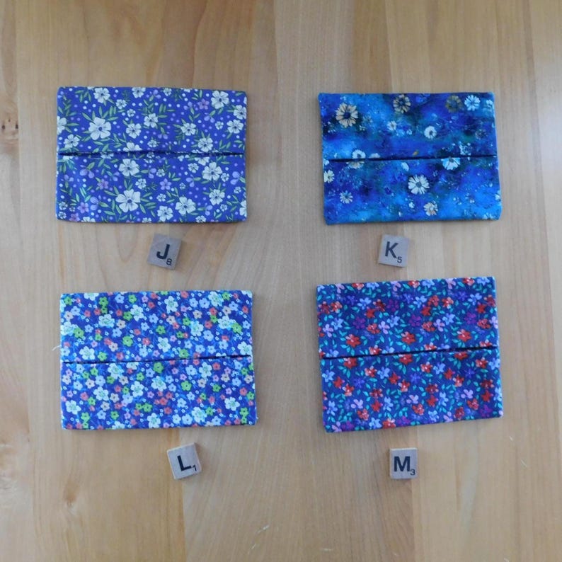 May include: Four rectangular fabric tissue holders featuring floral patterns. Top left J8 is purple with white flowers. Top right K5 is blue with white daisies. Bottom left L1 is light blue with tiny flowers. Bottom right M3 is dark blue with red and purple flowers.
