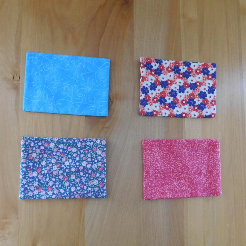 May include: Four rectangular fabric pouches arranged in a grid. The top left is light blue with a swirling line pattern. The top right features a red, white, and blue floral print. The bottom left is dark blue with small pink flowers. The bottom right is pink.