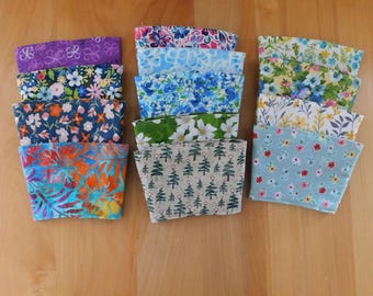 May include: A collection of twelve fabric cup sleeves arranged in three columns, featuring various patterns including floral prints in purple, blue, orange, and yellow, as well as a green leaf design and a beige print with small green pine trees.