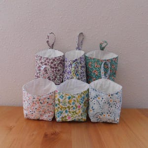 May include: Six fabric hanging storage baskets with various floral patterns in shades of purple, green, pink, yellow, and blue. Each basket features a white interior lining and a single fabric loop at the top for hanging, arranged in two rows.