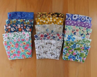 May include: A collection of fifteen fabric cup sleeves arranged in three columns, featuring various patterns including floral prints in blue, pink, yellow, and green, a white background with a dog print, and a yellow background with white flowers.