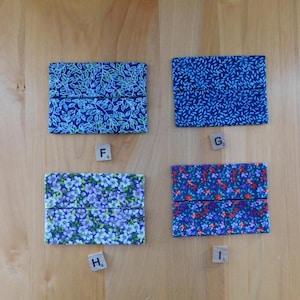 May include: Four rectangular fabric pouches with distinct patterns: top left features blue and green leaves, top right has a dark blue rice grain print, bottom left displays light purple flowers, and bottom right shows a dense floral pattern in red and blue.