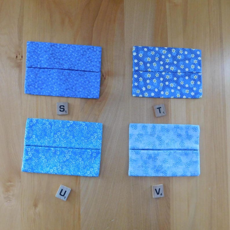 May include: Four rectangular fabric pouches in various shades of blue with floral patterns. Each pouch features a horizontal centre opening. The pouches are labelled with individual wooden letter tiles marked S, T, U, and V, each with a subscript number.
