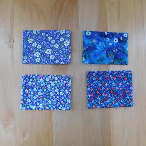 May include: Four rectangular fabric coasters featuring distinct floral patterns. The top left has white flowers on a blue background, the top right has a blue mottled floral print, the bottom left has small multi-coloured flowers, and the bottom right has red and blue flowers.