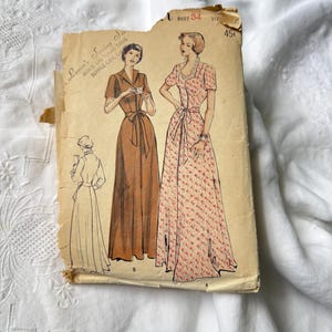 May include: Vintage sewing pattern featuring illustrations of two long dresses with short sleeves and a third sketch. The pattern is labeled "Laura's Sewing Service" and includes the bust size "34". The price is marked as "45¢".