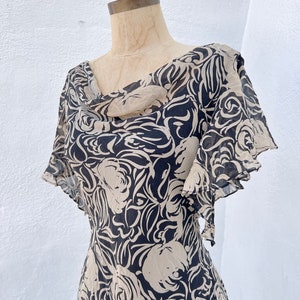 Pu&ograve; includere: Un abito vintage con un motivo floreale nero e beige. L'abito presenta uno scollo a cascata e maniche corte a balze. Il tessuto sembra leggero e fluido, ideale per la stagione calda.
