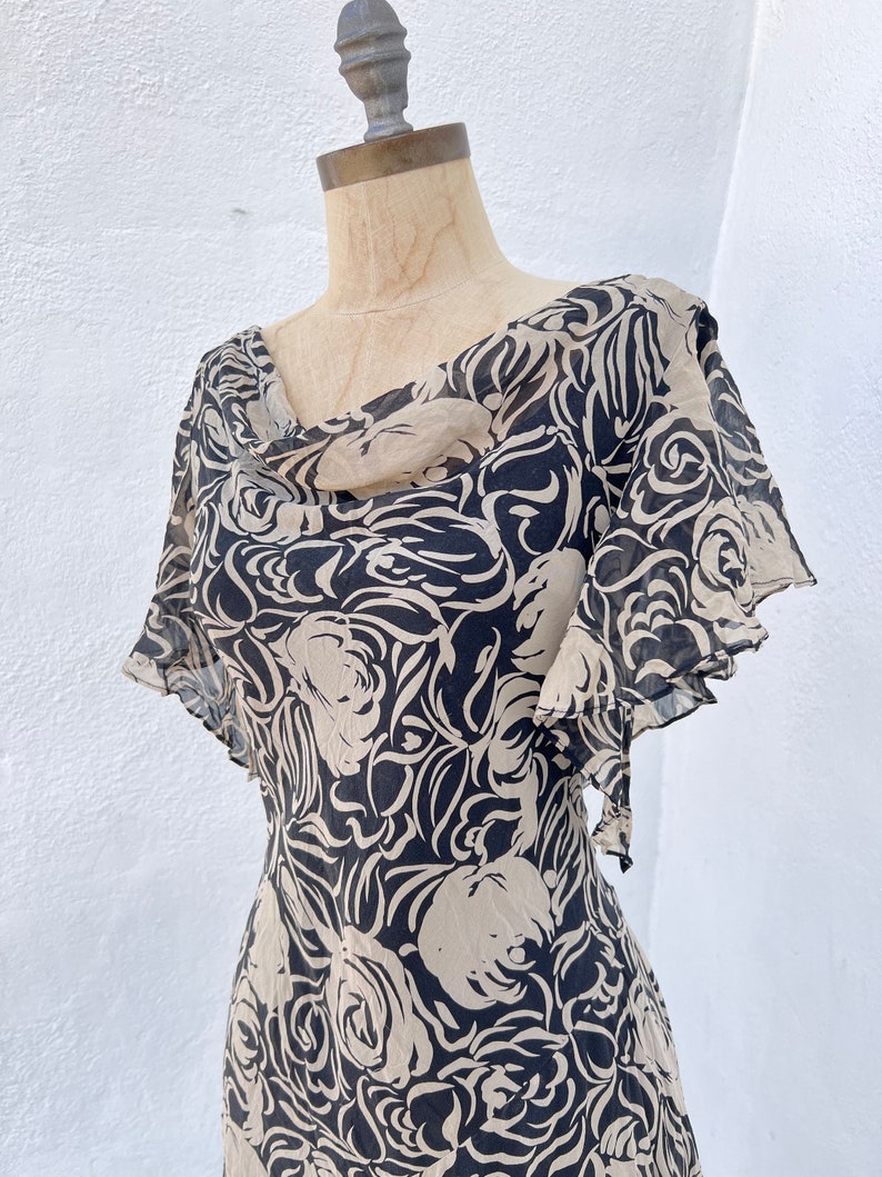 Pu&ograve; includere: Un abito vintage con un motivo floreale nero e beige. L'abito presenta uno scollo a cascata e maniche corte a balze. Il tessuto sembra leggero e fluido, ideale per la stagione calda.