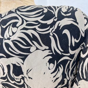 Pu&ograve; includere: Primo piano di un tessuto fantasia nero e crema. Il design presenta forme organiche a vortice in crema su sfondo nero. Il tessuto &egrave; drappeggiato su un manichino, mostrando il flusso del motivo.