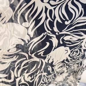 Pu&ograve; includere: Primo piano di un tessuto con un motivo floreale ripetuto. Il design presenta fiori e forme di foglie bianche stilizzate su uno sfondo blu navy scuro. Il tessuto sembra leggero e semitrasparente.