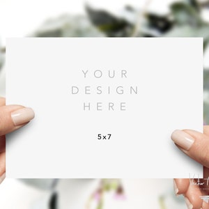 Puede incluir: Una tarjeta blanca de 5 x 7 pulgadas (12,7 x 17,8 cm) sostenida por dos manos. La tarjeta tiene el texto "YOUR DESIGN HERE" en una fuente gris claro. El fondo est&aacute; borroso con follaje verde.