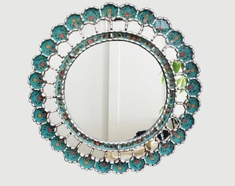 May include: A round mirror with a decorative turquoise and silver frame. The frame is adorned with floral designs in shades of pink, yellow, and green.