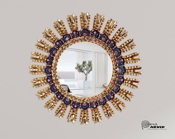 Op de afbeelding: Een ronde gouden spiegel met een blauw en wit mozaïekontwerp. De spiegel heeft een zonnestralenpatroon rond de rand.
