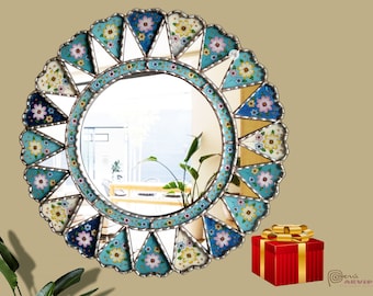May include: A round wall mirror featuring a decorative frame composed of triangular and scalloped segments painted with blue, white, and yellow floral patterns. The mirror has a central circular glass pane and a metallic border finish.