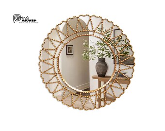 Op de afbeelding: Een ronde, goudkleurige spiegel met een decoratief parelrandje. De spiegel reflecteert een kamer met een vaas met groen en een fotolijst aan de muur.
