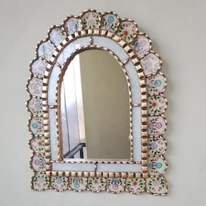 May include: A decorative arched mirror with a white and gold frame. The frame is made of small, scalloped pieces of glass with floral designs in shades of pink, blue, and green.