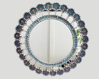 May include: A round mirror with a decorative frame. The frame is made of wood and is painted in shades of blue, gold, and pink. The frame has a floral design with intricate details.