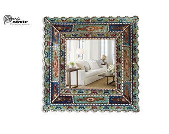 May include: A square mirror with a decorative, multi-colored frame. The frame is made of small, intricately patterned tiles in shades of blue, green, red, and gold. The mirror reflects a modern living room with a white sofa and a coffee table.