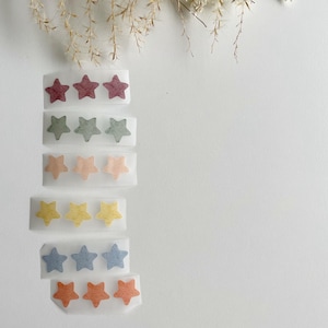 Könnte beinhalten: Ein Satz von sechs Streifen aus transparentem Klebepapier mit jeweils drei Filzstern-Aufklebern. Die Sterne sind in verschiedenen Farben: rot, grün, pfirsich, gelb, blau und orange.