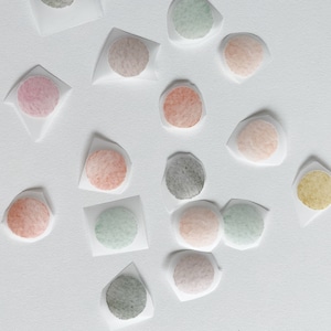 May include: Assortment of round watercolor paint swatches on white paper. The colors include pink, red, orange, yellow, green, blue, and gray.