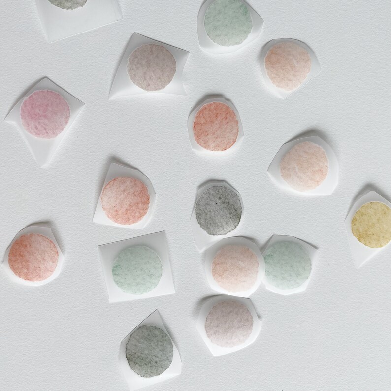 May include: Assortment of round watercolor paint swatches on white paper. The colors include pink, red, orange, yellow, green, blue, and gray.
