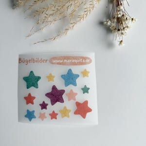 Könnte beinhalten: Ein Bogen mit bunten, sternförmigen Bügelbildern in verschiedenen Größen und Farben, darunter Grün, Gelb, Blau, Lila und Orange. Der Text "Bügelbilder" und "www.mariequita.de" ist auf dem Bogen aufgedruckt.