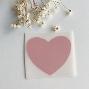Könnte beinhalten: Ein rosa herzförmiger Aufkleber auf weißem Hintergrund.