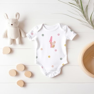 May include: White baby onesie with pink and gold polka dots and a pink number one with a mouse illustration.