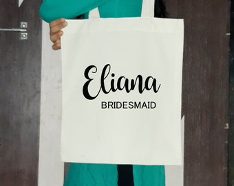 May include: White tote bag with black text that reads "Eliana Bridesmaid".