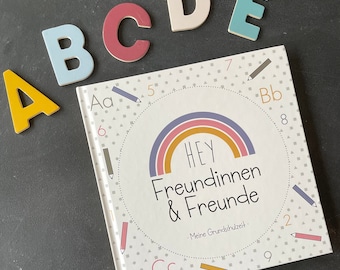 May include: A colorful book titled "HEY Freundinnen & Freunde - Meine Grundschulzeit" with a rainbow design and a circle of numbers and letters around the rainbow. The letters A, B, C, D, and E are displayed in different colors on a black background.