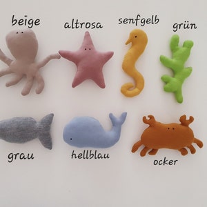 Könnte beinhalten: Ein Set mit 8 Plüschtieren in Form von Meeresbewohnern. Die Tiere sind beige, rosa, gelb, grün, grau, hellblau und orange. Die Tiere sind mit ihren Farben in Deutsch beschriftet.