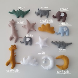 Könnte beinhalten: Ein Set mit 12 Plüschtieren in verschiedenen Farben und Formen, darunter eine Giraffe, ein Elefant, ein Krokodil, ein Nashorn, ein Stern, eine Wolke und ein Halbmond. Die Spielzeuge sind aus weichem Stoff gefertigt und haben gestickte Details. Die Farben umfassen Beige, Grau, Braun, Grün, Blau, Weiß und Gelb.
