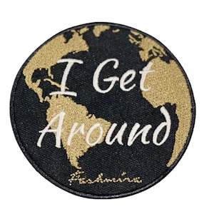 May include: Round black patch with a gold-colored world map design. The words "I Get Around" are embroidered in white, with the brand name "Kashmira" at the bottom. The patch is likely for travel or adventure.