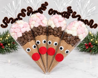 May include: Four clear cone-shaped plastic bags filled with layers of brown cocoa powder, chocolate chips, and pink and white mini marshmallows. Each bag features two plastic googly eyes, a red felt nose, and brown pipe cleaner antlers.